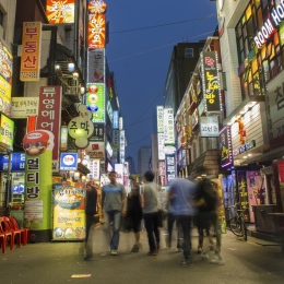 En koreansk storstad på kvällen, med lysande skyltar och människro på en gågata