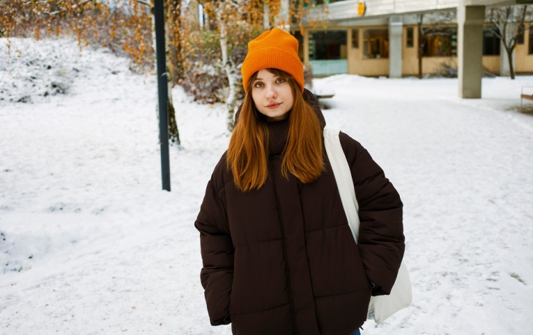 En tjej med orange mössa på ett snöigt campus.